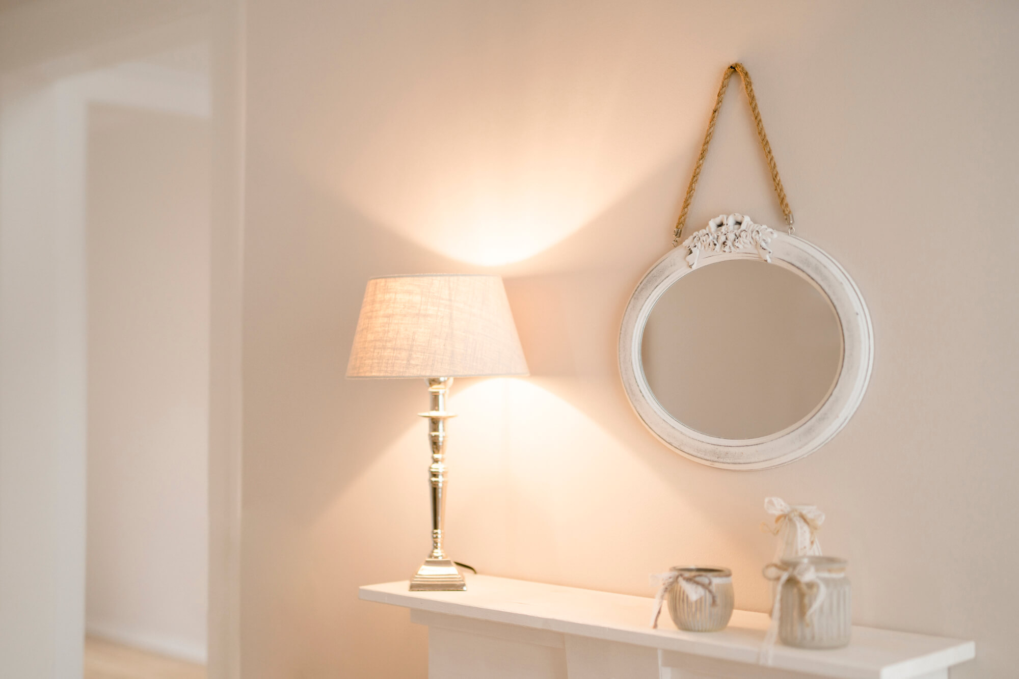 Lisa Treusch Mainz Immobilienfotografin Immobilienfotograf Nahaufnahme eines weißen runden Spiegels mit einer braunen Kordel und einer Stehlampe mit silbernem Fuss und weißem Lampenschirm Home-Staging